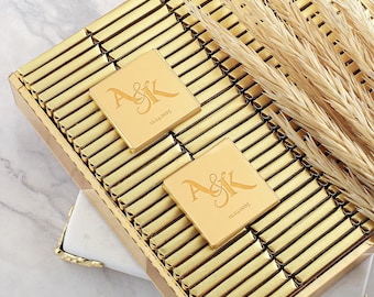 Könnte beinhalten: Eine goldene Schachtel gefüllt mit einzeln verpackten Schokoladentafeln. Die Schokoladentafeln sind mit einer goldenen Folie umhüllt und mit den Initialen "A&K" und dem Datum "12.24.2025" personalisiert.