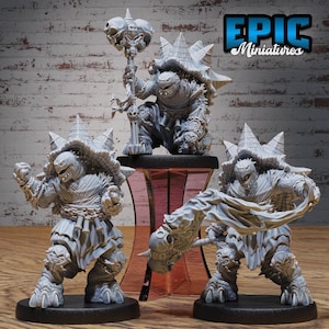 May include: Three grey miniature fantasy figures of turtle-like creatures. One figure kneels holding a skull-topped mace, while the other two stand in dynamic poses, one with a weapon and the other with a raised fist. The figures have detailed armour and shell features.