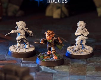 May include: Three miniature fantasy figures, each on a circular base, are displayed. The figures are in shades of gray and brown, with one in the center holding a sword. The text "NIGHTDAGGER ROGUES" is at the top.