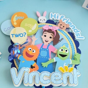 Puede incluir: Un adorno colorido para pastel de cumpleaños con personajes de dibujos animados y el nombre "Vincent". El diseño incluye una niña, dos marionetas y las palabras "Hi Friends!" y "Can you say TWO?" en globos.