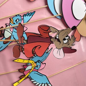 May include: A set of six colorful paper cutouts of cartoon characters on sticks. The characters include a mouse wearing a red coat, a blue bird, and a pink and white bird. The characters are perfect for a children's party or for use as props in a play.