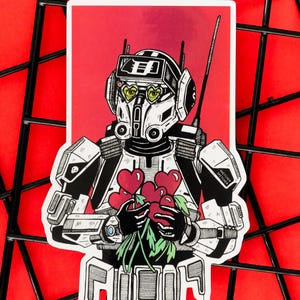 Pode incluir: Um autocolante com um robô com capacete e olhos em forma de coração, segurando um buquê de flores vermelhas em forma de coração. O robô é preto e branco com detalhes verdes, sobre um fundo vermelho. A palavra "FIQOS" está na parte inferior.