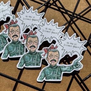 以下が含まれることがあります： 緑色の制服と赤いリボンを着けた、厳しい表情の人物の漫画イラストが描かれたステッカーのセット。各ステッカーには「HE HAD US DISOBEY ORDERS！」というテキストとアーティストのサインが入った吹き出しが付いています。