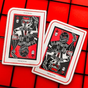 Puede incluir: Dos naipes con un diseño rojo, negro y blanco. Las cartas presentan una ilustración estilizada de una figura con casco que sostiene un arma. El fondo es rojo con un patrón de cuadrícula negra.