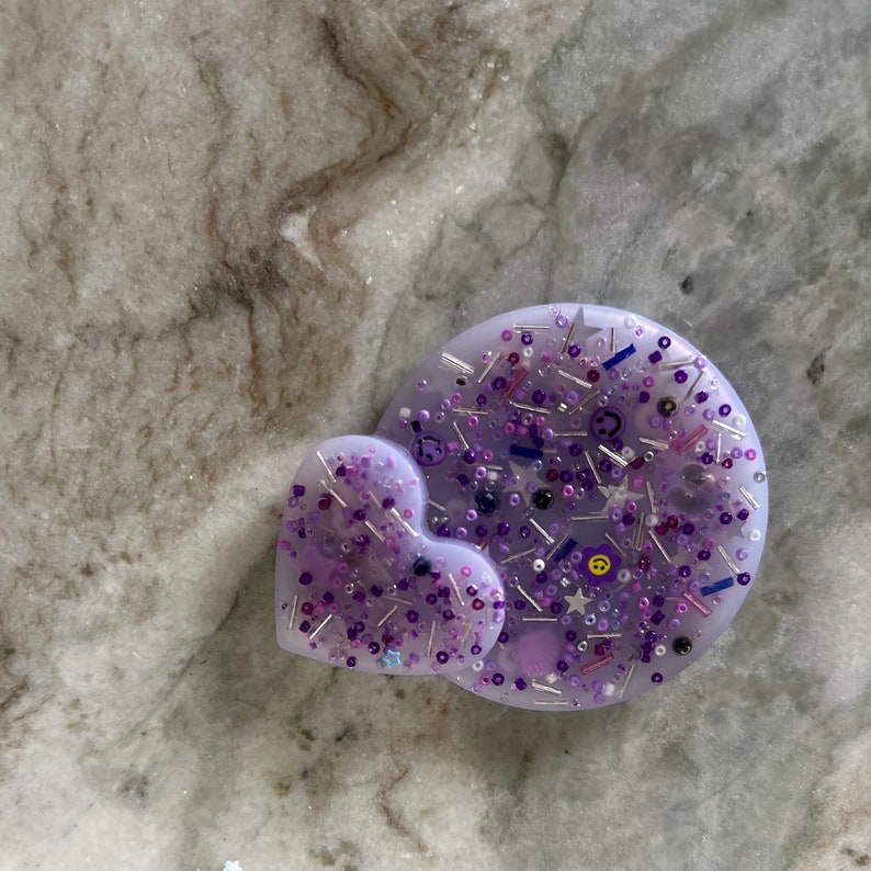 May include: A purple resin heart and circle with embedded glitter, silver beads, and small purple, blue, and yellow charms.