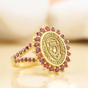 May include: A gold ring with a red stone setting. The ring features the University of Texas at San Antonio seal with the words "The University of Texas at San Antonio" and "Praesidium Civitatis Disciplina" around the seal.