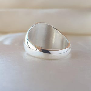 May include: A polished silver ring with a smooth, rounded band and a wide, flat top surface. The interior of the band features a small, clear engraving of the number 925, indicating the metal composition of this solid, reflective silver jewelry piece.