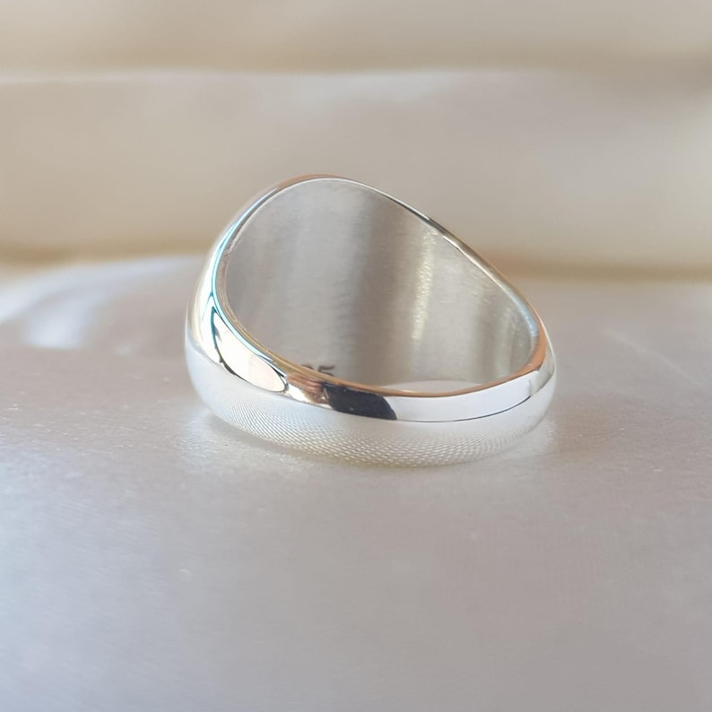 May include: A polished silver ring with a smooth, rounded band and a wide, flat top surface. The interior of the band features a small, clear engraving of the number 925, indicating the metal composition of this solid, reflective silver jewelry piece.