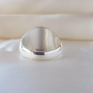 May include: A polished silver ring with a smooth, rounded band and a wide, flat top surface. The interior of the band is clearly stamped with the hallmark 925, indicating the sterling silver composition of this circular piece of jewelry.