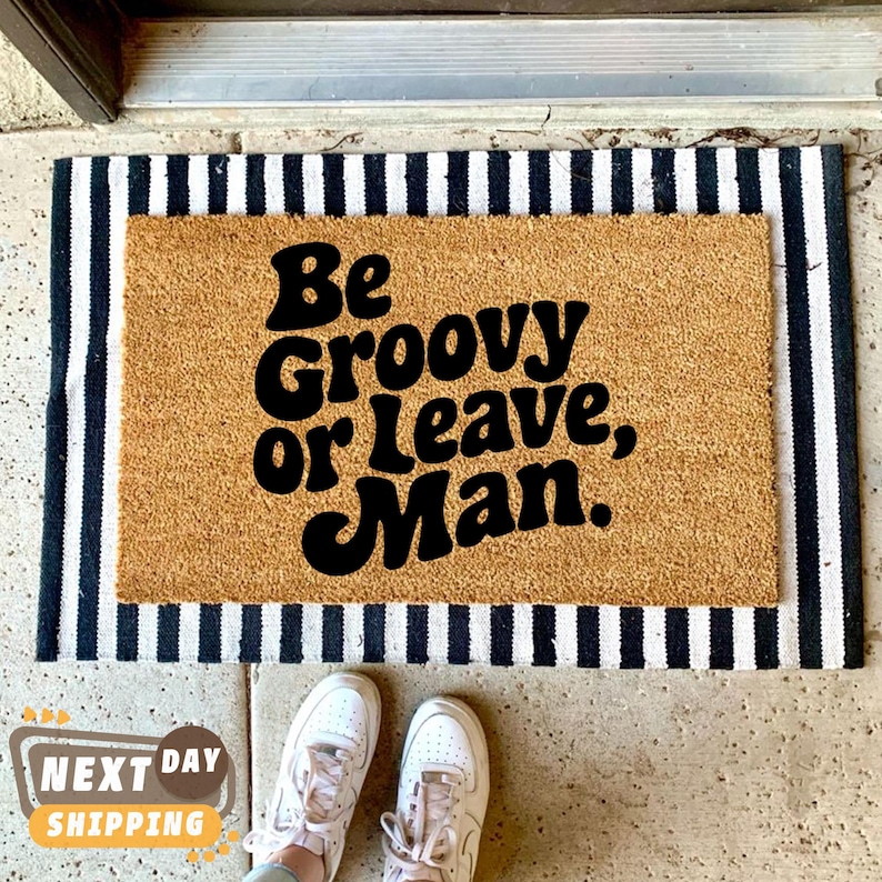 May include: A brown coir doormat with black text that reads "Be Groovy or Leave, Man."