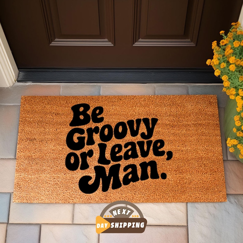 May include: A brown coir doormat with the text "Be Groovy or Leave, Man." in black lettering.