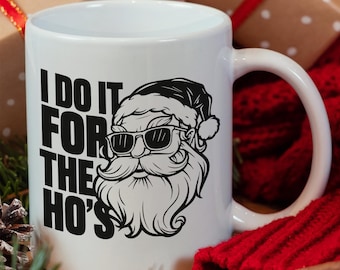 May include: White ceramic mug with a black and white illustration of Santa Claus wearing sunglasses. The text "I do it for the ho's" is printed on the mug.