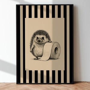 May include: A framed wall art print featuring a detailed illustration of a hedgehog holding a roll of toilet paper. The artwork is set against a beige background with a vertical black and beige striped border, all enclosed in a thin black frame.
