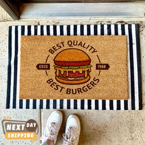 May include: A brown coir doormat with black and white stripes. The doormat has a graphic of a hamburger with the text "Best Quality Best Burgers" and "Estd 1988" around it.