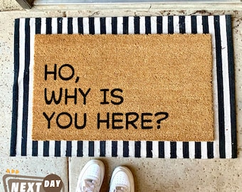 May include: A brown coir doormat with black and white striped edging. The doormat has the text "HO, WHY IS YOU HERE?" printed in black.