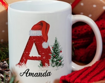 May include: White ceramic mug with a red letter A decorated with a Santa hat and a small Christmas tree. The mug is personalized with the name "Amanda".