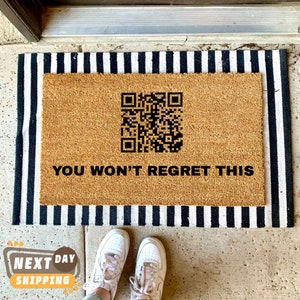 May include: A brown coir doormat with black and white striped border. The doormat has a black QR code and the text "YOU WON'T REGRET THIS" printed on it.