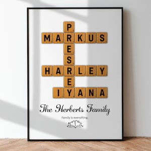 May include: A framed print with a white background featuring the names "Markus", "Harley", "Iyana", and "P" spelled out using wooden Scrabble tiles. The text "The Herberts Family" and "Family is everything." is printed below the tiles.