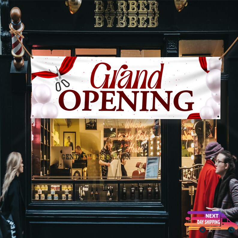 May include: A white banner with red accents and the text "Grand Opening" in red lettering. The banner is hanging above a shopfront with a sign that reads "Barber Bybber".