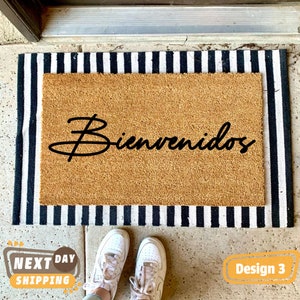May include: A brown coir doormat with black and white striped edging. The doormat has the word "Bienvenidos" written in black cursive script.