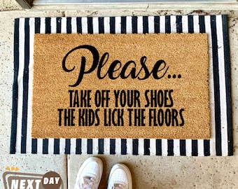 May include: A brown coir doormat with black and white striped border. The doormat has the text "Please... Take off your shoes the kids lick the floors" printed in black.