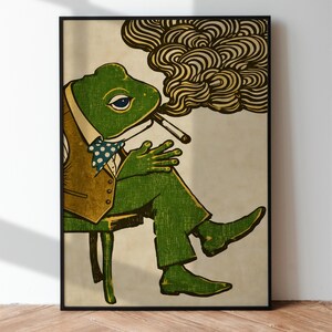 May include: A framed art print featuring a green frog in a suit, smoking a cigarette. The frog is seated on a chair, with a brown vest and a blue polka-dot bow tie. The background is a neutral beige with a swirl of smoke.