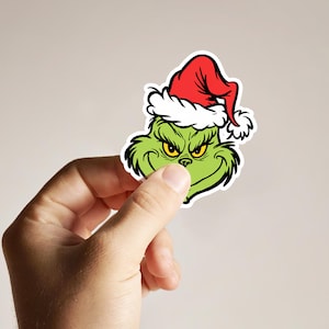 May include: A green Grinch character wearing a red and white Santa hat. The Grinch is smiling with a mischievous look on his face.