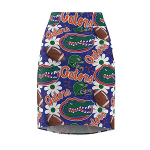 May include: A blue pencil skirt with a repeating pattern of the word "Gators", footballs, green helmets, and a cartoon alligator head with the word "Gators" in orange. White daisy flowers are also part of the pattern.