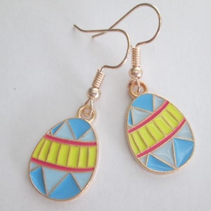 May include: A pair of gold dangle earrings with blue, yellow, and red enamel egg-shaped charms. The eggs have a geometric pattern.