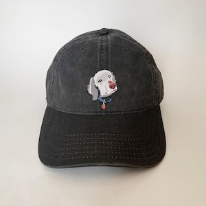 May include: Black baseball cap with a white dog embroidered on the front. The dog has a blue collar and a red heart charm.