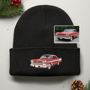 May include: Black knit beanie featuring an embroidered red classic car design. The car has white accents and is set against a black background. A smaller image of the car is also present. The beanie is a winter accessory.