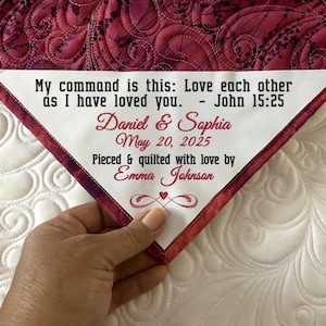May include: A personalized quilt with a white triangular patch featuring the names "Daniel & Sophia" and the date "May 20, 2025." The patch also includes the quote "My command is this: Love each other as I have loved you. - John 15:25." The quilt is pieced and quilted with love by Emma Johnson.