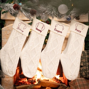 May include: Four white knitted Christmas stockings with red embroidered dog outlines and names: Sterling, Penny, Cooper, and Poppy.