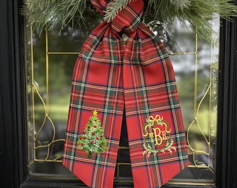 May include: A red plaid Christmas door decoration with a green Christmas tree and gold star embroidery. The decoration also features a gold monogram and is hanging on a glass door.