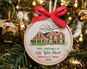 May include: Embroidered Christmas ornament featuring a house design with the text "First Christmas at 1210 Tyler Street Rebecca & James 2025". The ornament has a red ribbon and is hanging on a Christmas tree.