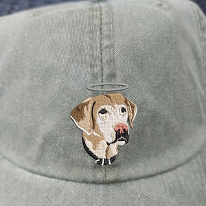 May include: A green baseball cap featuring an embroidered image of a dog with a halo. The dog is light brown with white markings and wears a black collar.