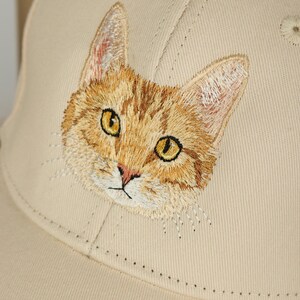 May include: A beige baseball cap with an embroidered image of a tabby cat's face.