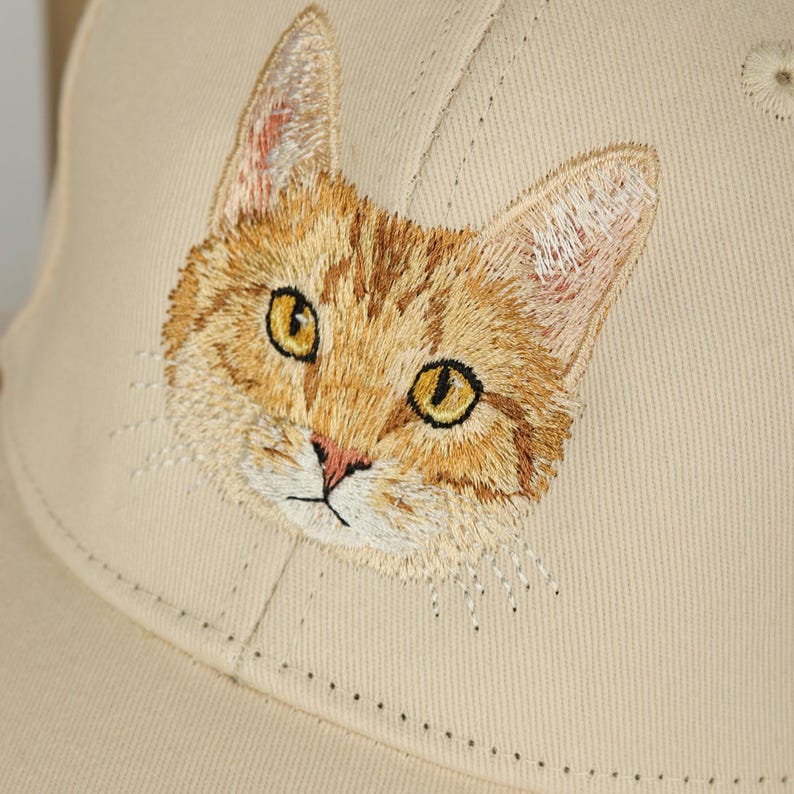 May include: A beige baseball cap with an embroidered image of a tabby cat's face.