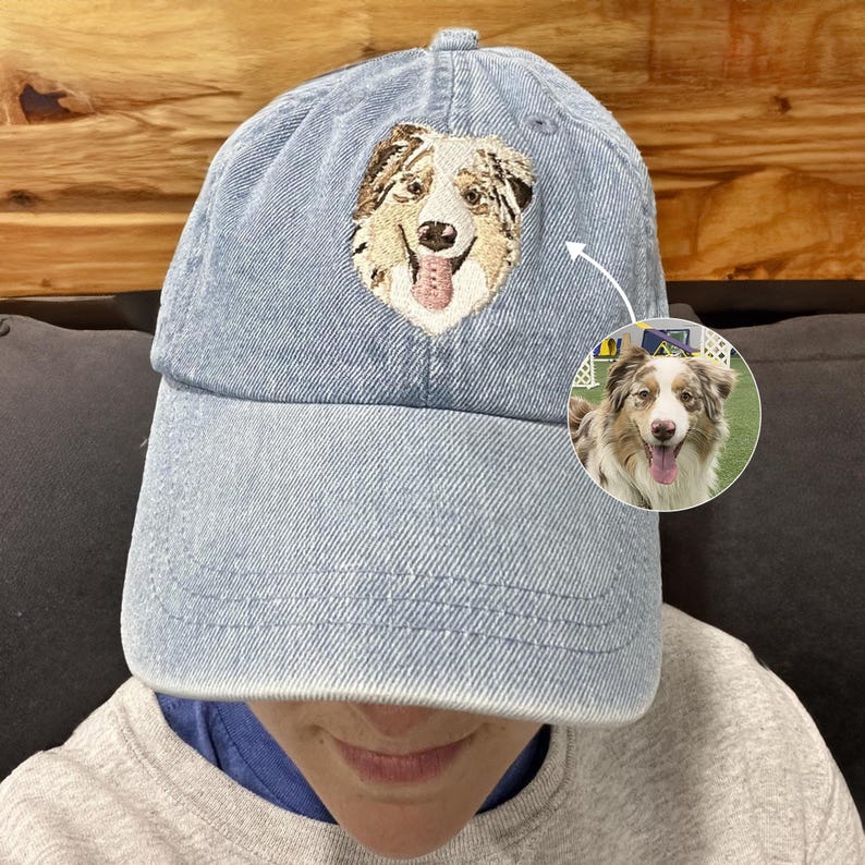 May include: A blue denim baseball cap with an embroidered image of a dog on the front. The dog is a brown and white Australian Shepherd with a pink tongue sticking out.