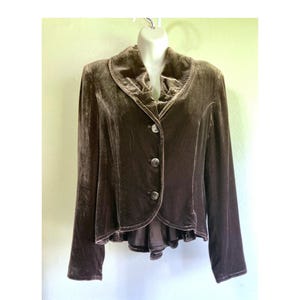 May include: A brown velvet jacket with a ruffled collar and three buttons. The jacket has long sleeves and a slightly flared bottom. The fabric has a soft, lustrous appearance, suggesting a formal or elegant style.