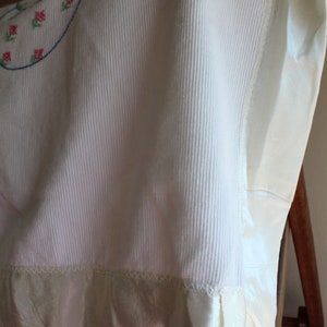 May include: A white crocheted baby blanket with a satin trim and embroidered flowers.