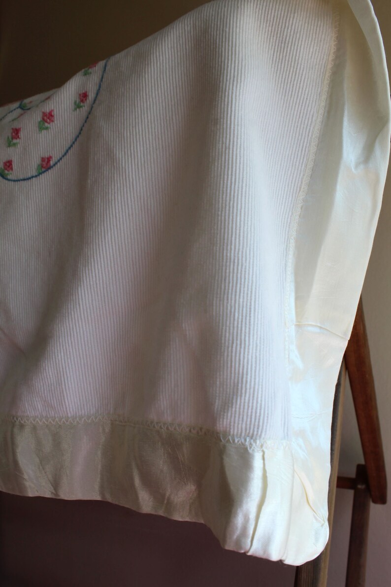 May include: A white crocheted baby blanket with a satin trim and embroidered flowers.