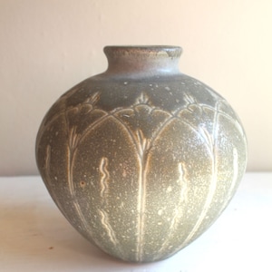 Può includere: Un vaso in ceramica verde con un designo testurizzato e in rilievo. Il vaso ha un corpo arrotondato e un'apertura stretta.