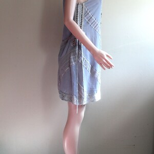 May include: A light blue sleeveless dress with a lace overlay and a delicate pattern. The dress is on a white mannequin.