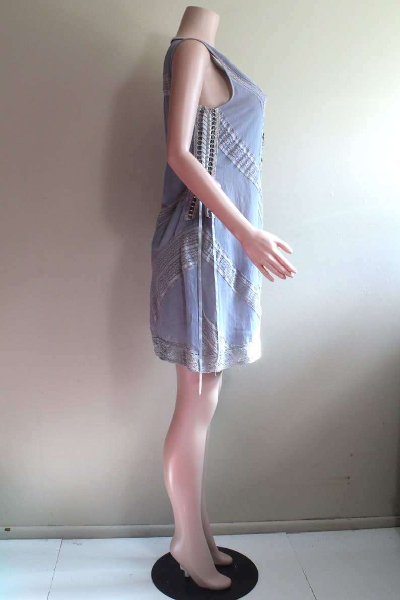 May include: A light blue sleeveless dress with a lace overlay and a delicate pattern. The dress is on a white mannequin.