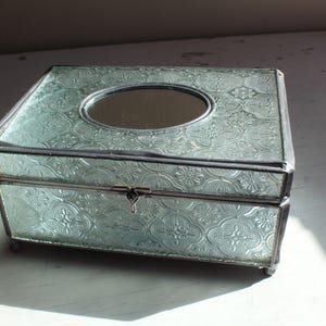 May include: A light blue glass jewelry box with a decorative floral pattern and a small mirror on the lid.