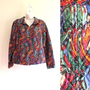 Pode incluir: Uma jaqueta acolchoada com uma estampa abstrata colorida em tons de vermelho, laranja, amarelo, verde, azul e preto. A jaqueta tem fecho de botões e mangas compridas.