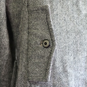 May include: A close-up of a grey tweed jacket with a black button on a flap pocket.