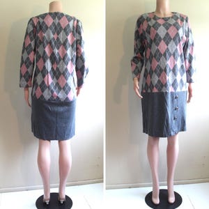 Könnte beinhalten: Ein graues und rosafarbenes Argyle-Musterkleid mit einem grauen Rock und drei Knöpfen an der Seite. Das Kleid hat lange Ärmel und einen runden Ausschnitt.