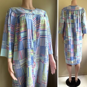 Peut inclure: Une robe d'intérieur arrivant au genou avec un motif patchwork composé de rayures et de carreaux bleus, verts, roses et jaunes. Le vêtement présente des manches trois-quarts, une encolure ronde et une fermeture boutonnée avec des boutons métalliques.